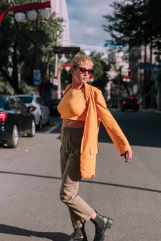 Stylish woman in orange blazer poses on a city street, showcasing a modern fashion look.