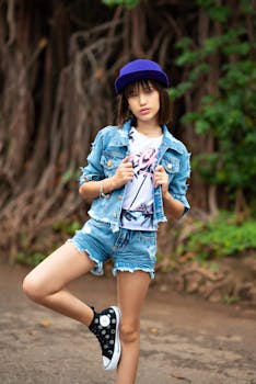 Stylish young girl posing outdoors in denim and a vibrant blue cap.