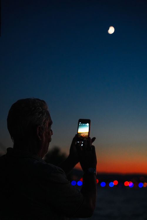 Free Silhouette of a man taking a photo of the night sky and moon with a smartphone. Stock Photo