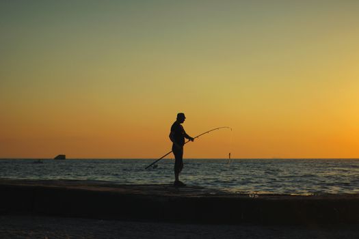 Silhouette of a man fishing at sunset on the beach in Odessa, Ukraine, creating a calming scene.