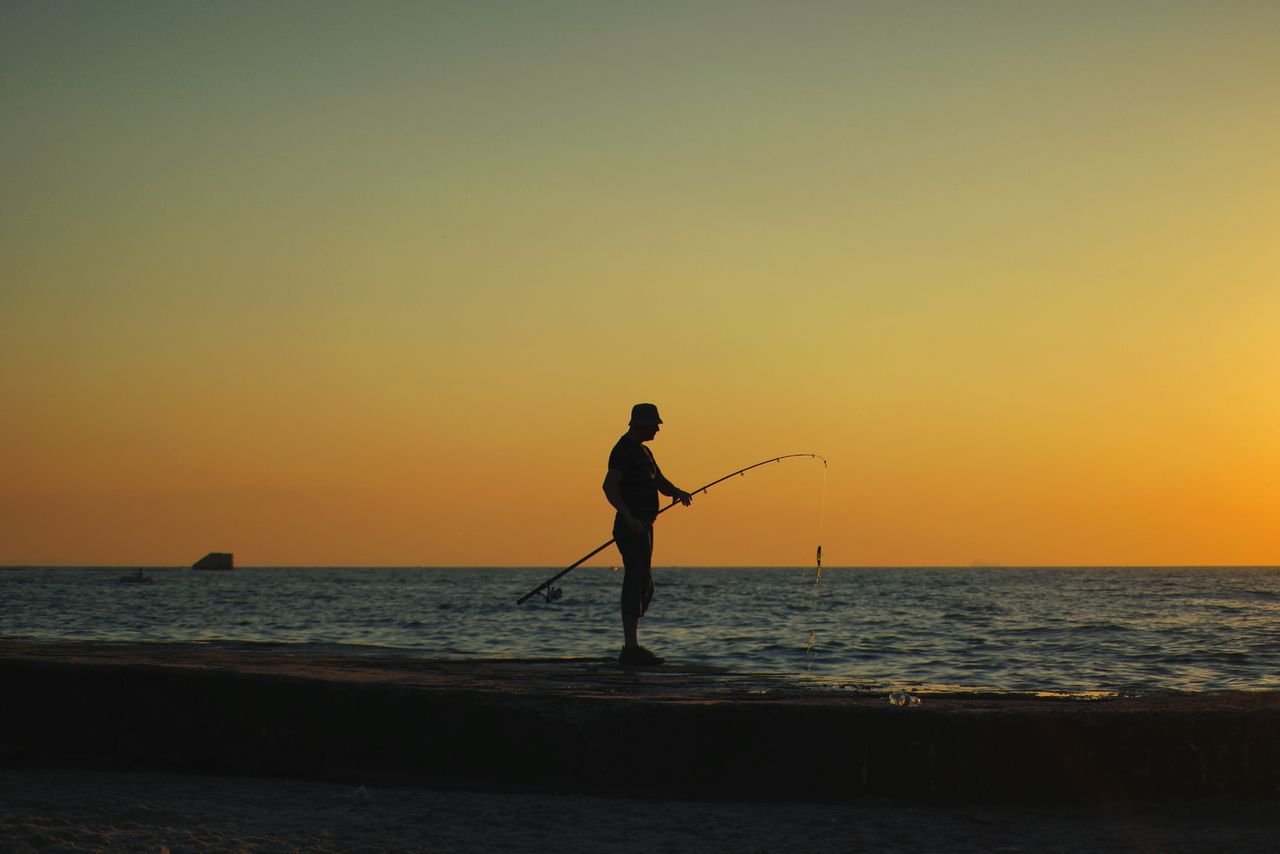 silhouette of a man fishing at sunset on the beach in odessa ukraine c