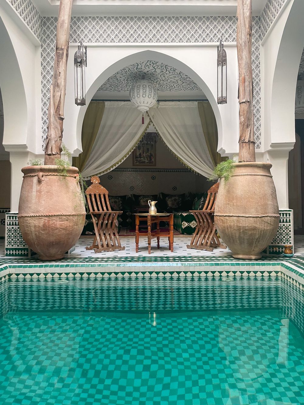 Two tall clay urns beside a tiled pool in front of a curtained pavilion