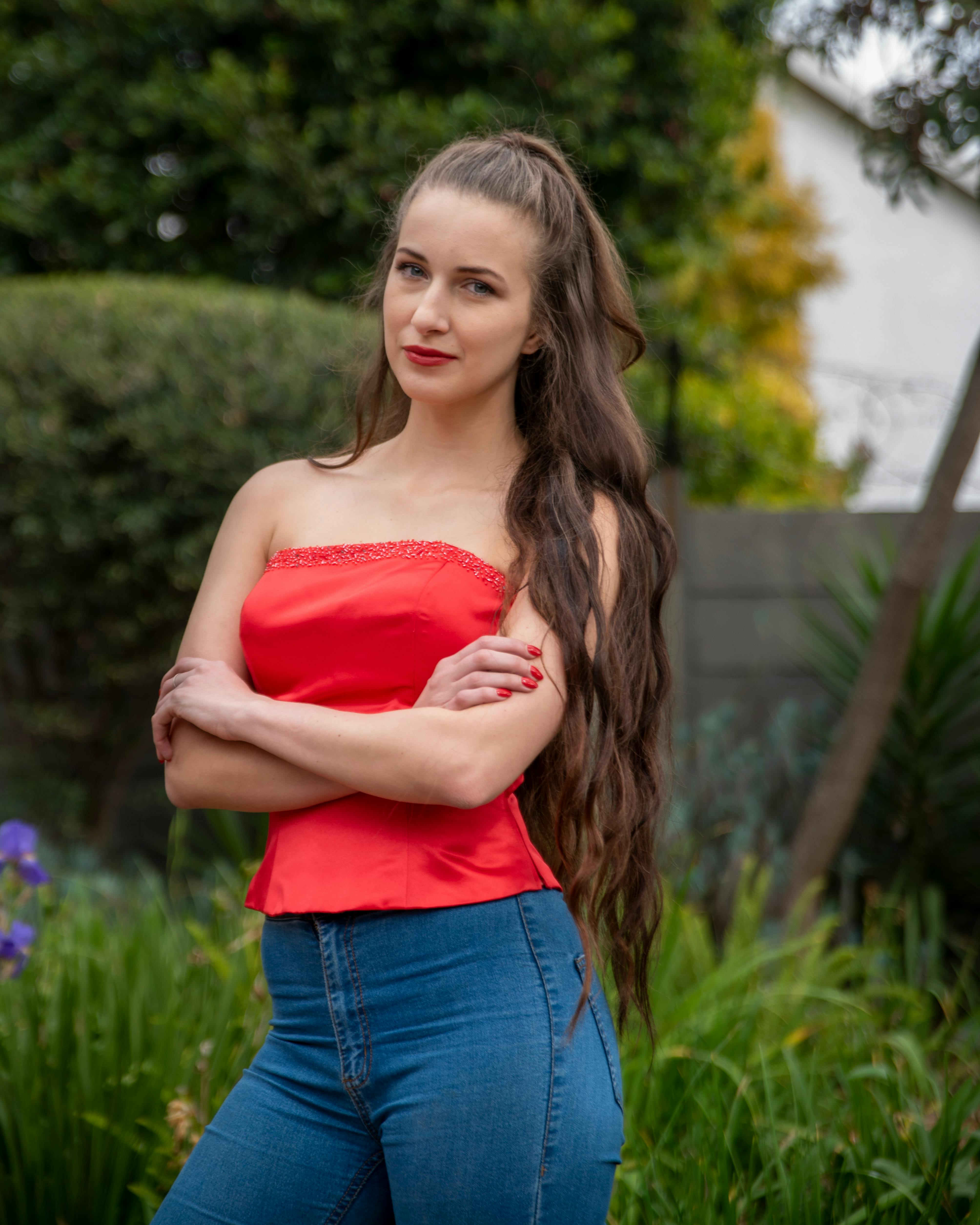 a woman in an orange tube top and denim pants is smiling and posing