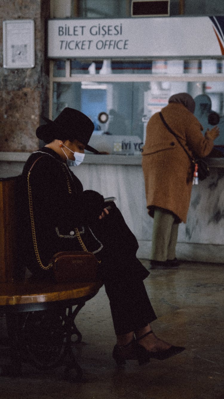 Man In Hat And Mask Sitting Near Ticket Office