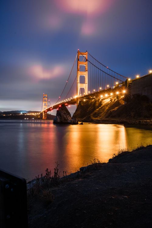 Free A stunning nighttime view of the illuminated Golden Gate Bridge in San Francisco casting reflections on the calm water. Stock Photo