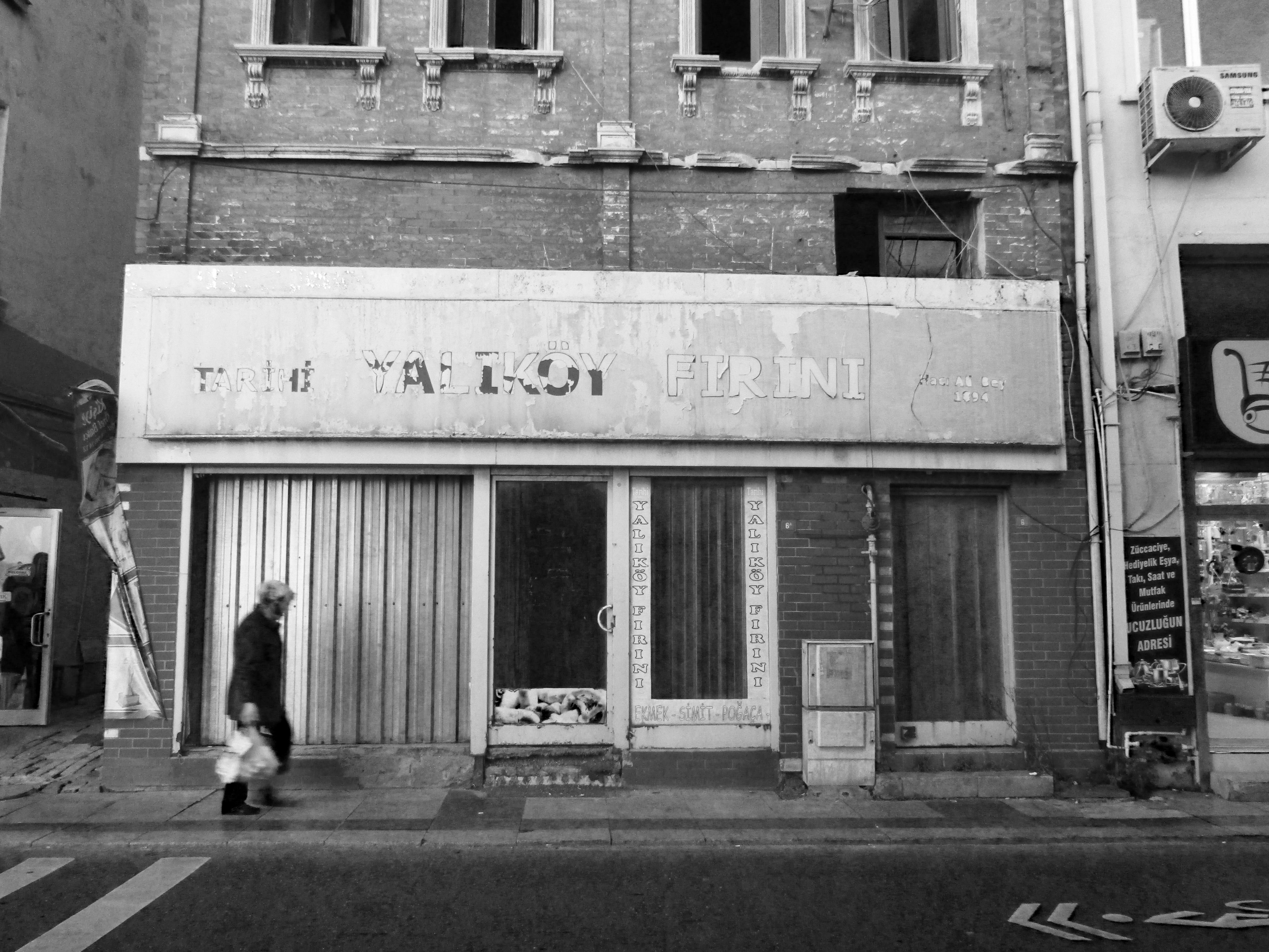 Monochrome street view of an old building with a person walking by.