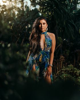 Elegant woman in tropical dress posing outdoors, surrounded by lush greenery.