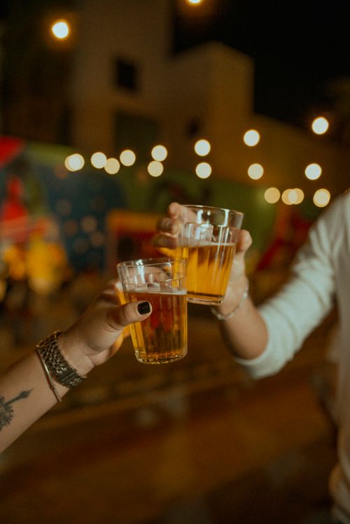 Free Two people toast with beer glasses outdoors at night, capturing a festive urban vibe. Stock Photo