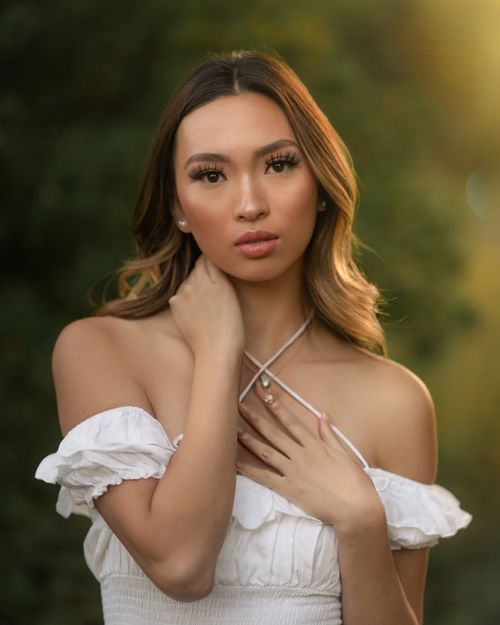 Free Portrait of a woman with long hair, posing with hand on neck in soft outdoor light. Stock Photo