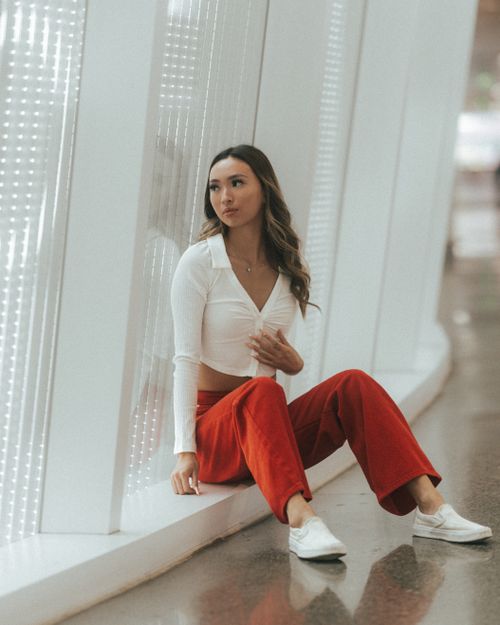 Free Fashionable woman in red pants and white top sitting indoors, exuding style and elegance. Stock Photo
