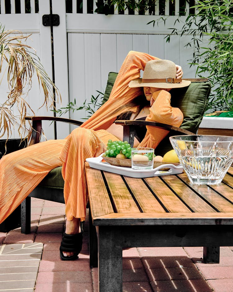 Fashion Woman In Hat And Orange Costume Sitting In Patio