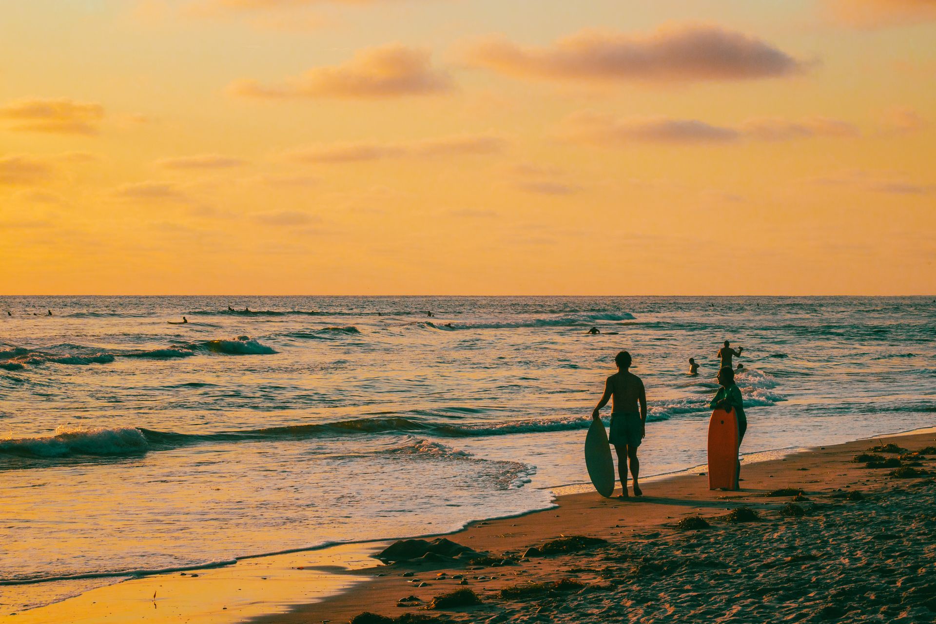 Surfistas caminando por la playa al atardecer, siluetas doradas
