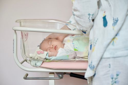 Free A tender moment of a newborn baby sleeping peacefully in a hospital bassinet being gently touched by a parent. Stock Photo