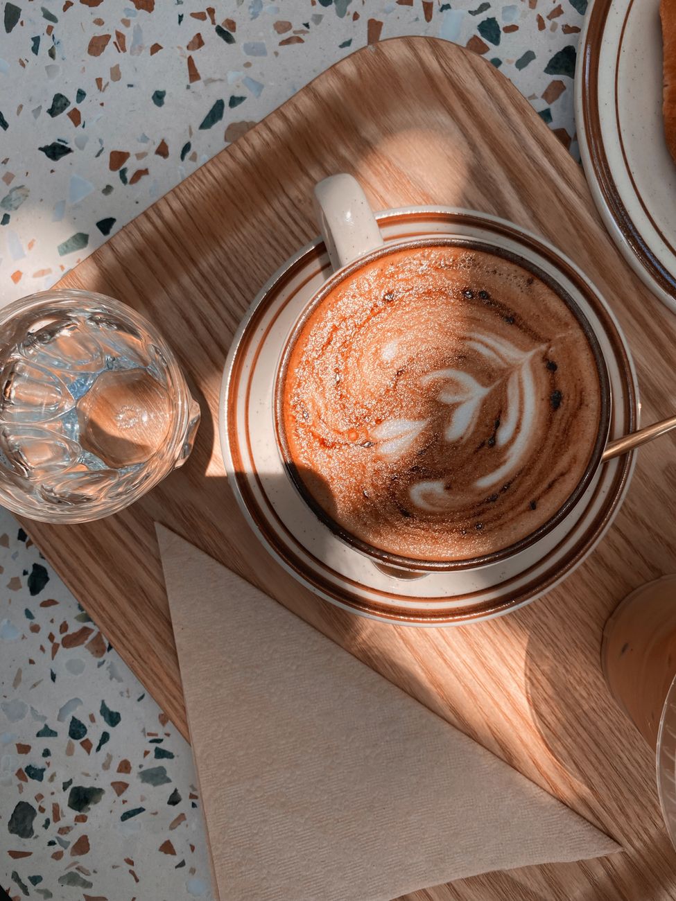 A top down view of a coffee with beautiful latte art placed on a wooden tray, capturing cozy café vibes.