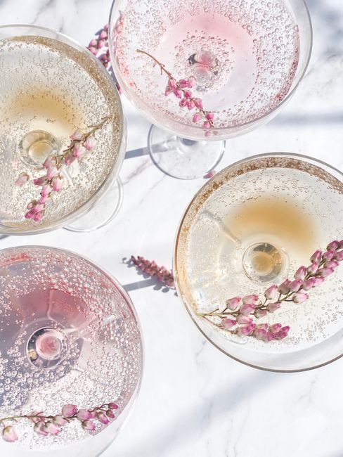 A top view of sparkling cocktails with floral garnishes in elegant glasses on a marble surface.