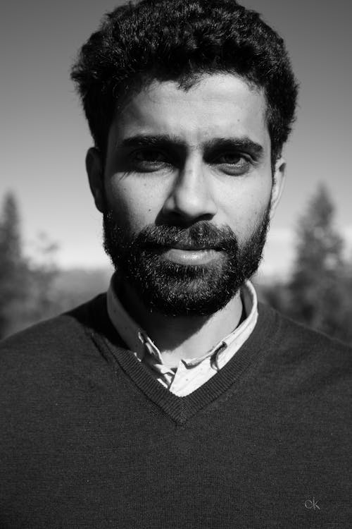 A Grayscale Photo of a Bearded Man in Black Shirt Looking with a Serious Face