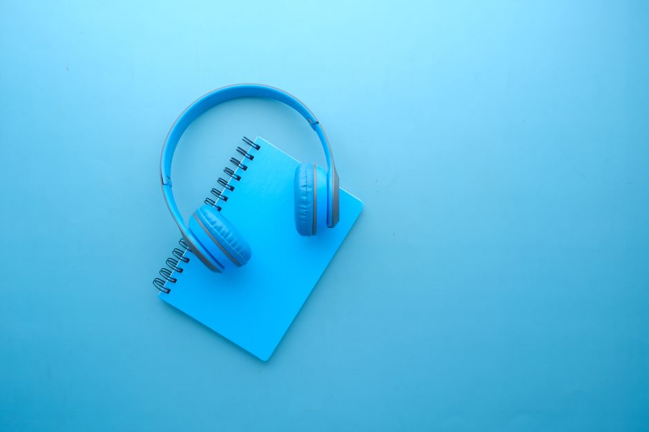 Minimalist flat lay of blue headphones and a notebook on a bright blue background.