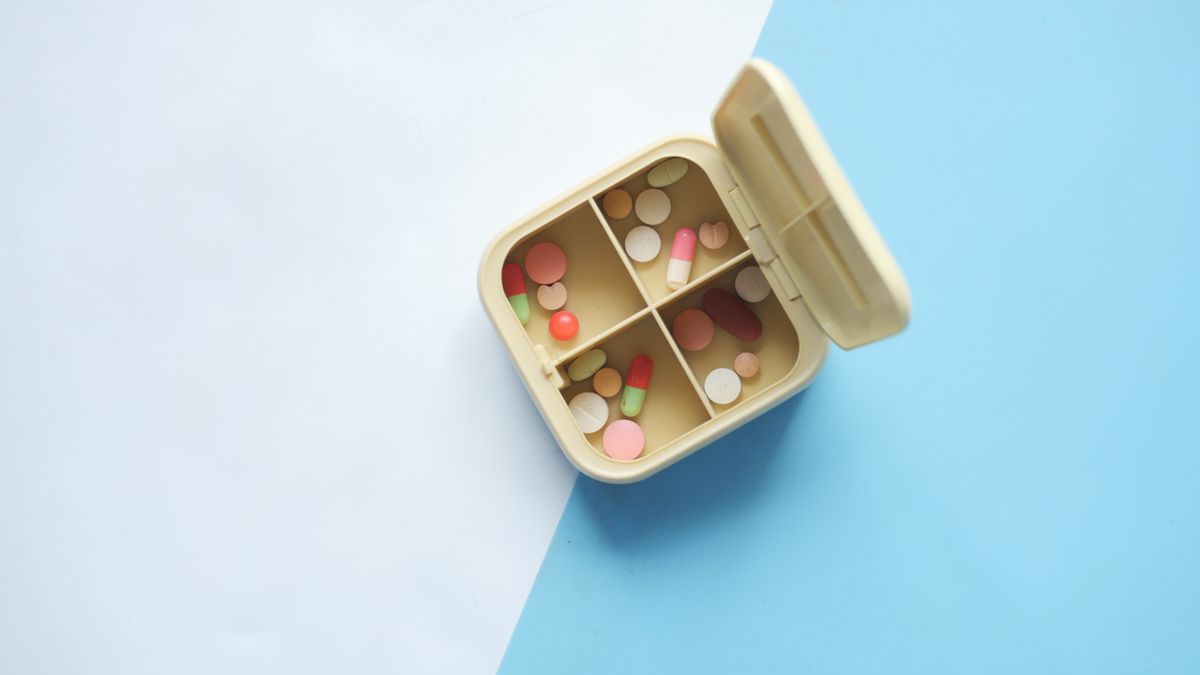 Top view of an open pill box filled with various pills and capsules on a blue and white background.