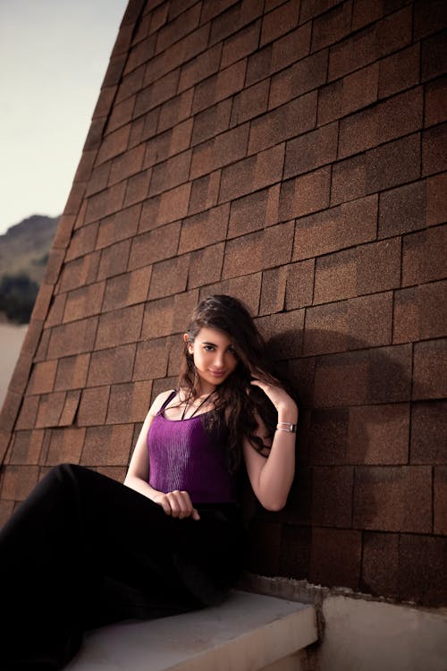 A Woman in Purple Tank Top Sitting while Leaning on the Wall