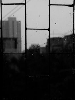 Raindrops on a window with a blurred cityscape in black and white, creating a moody atmosphere.