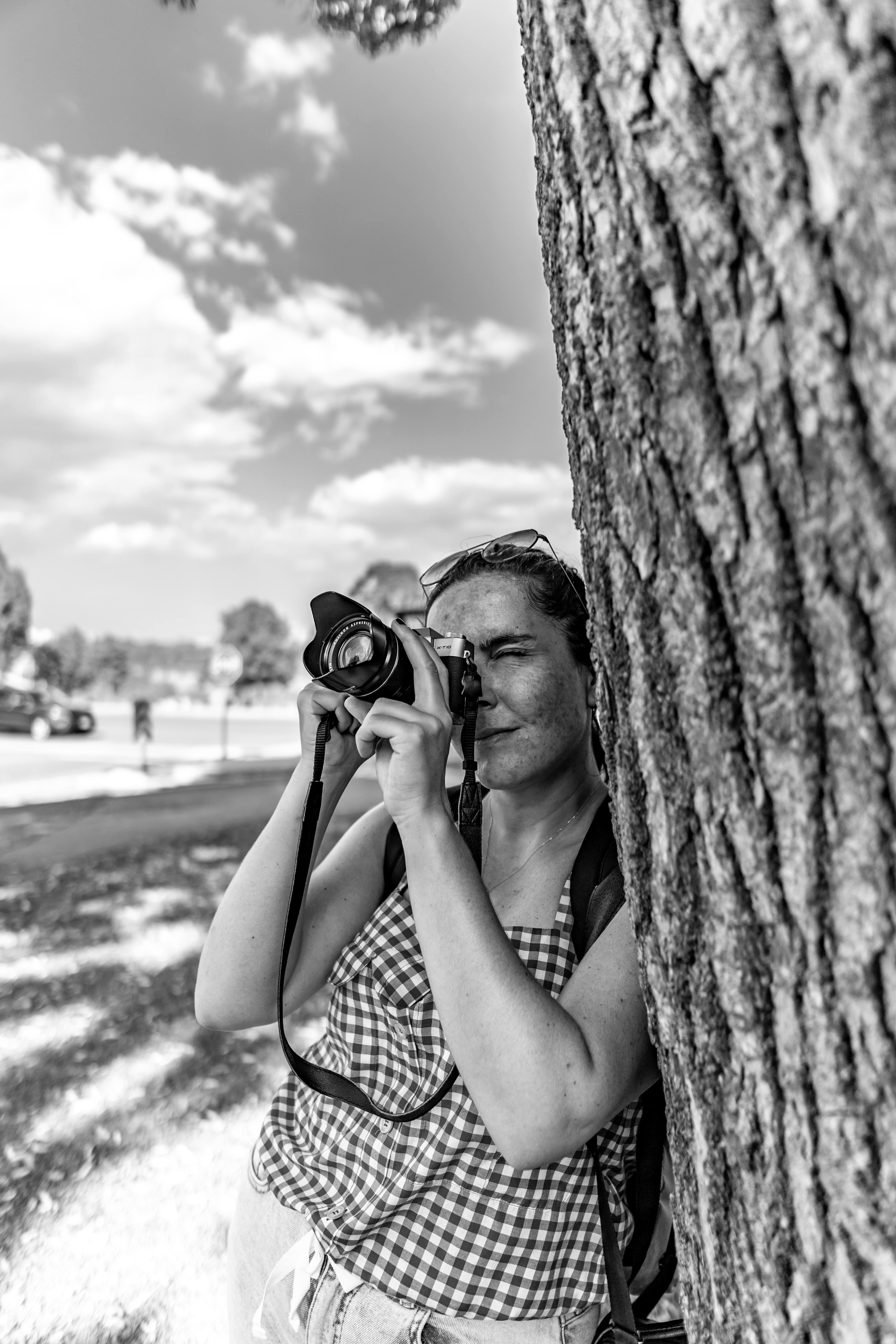 Monochrome image of a woman photographing Niagara Falls, leaning on a tree.