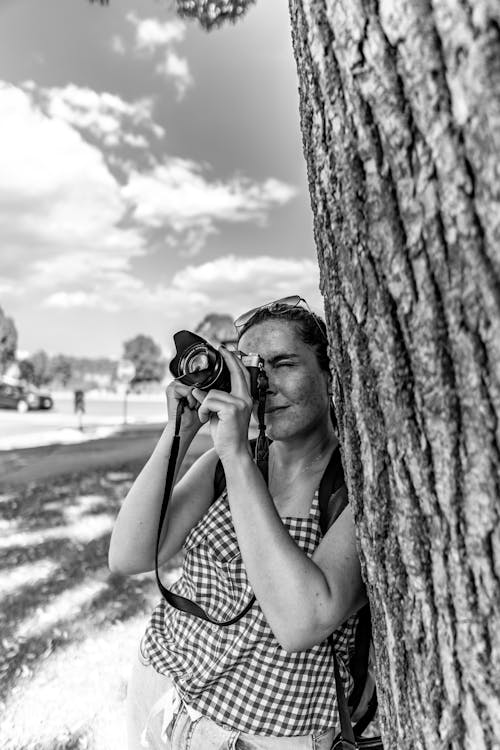 A Grayscale Photo of a Woman Leaning on the Tree while Holding a Camera
