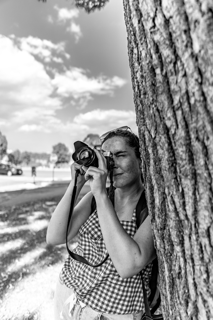 Monochrome image of a woman photographing Niagara Falls, leaning on a tree.