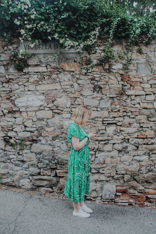 A Woman in Green Dress Standing Near the Stone Wall