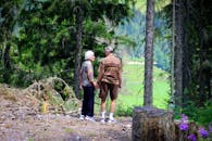 一对老年夫妇手牵着手，在宁静的森林小径上漫步，享受着大自然