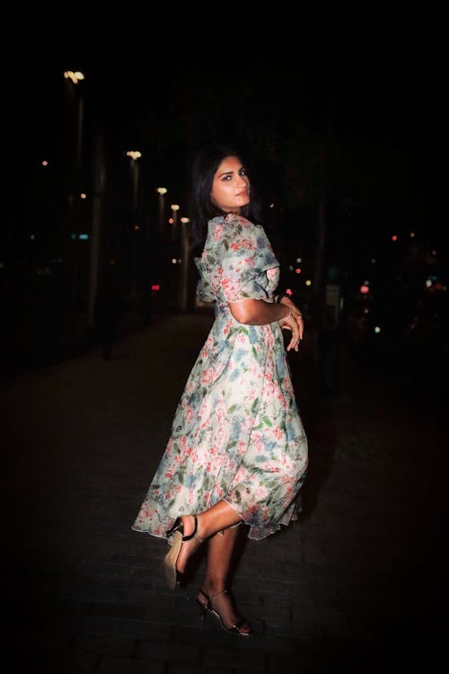 A Woman in Floral Dress Standing on the Street at Night