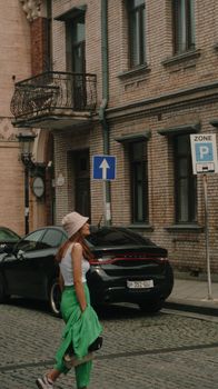 Woman walking in Batumi street, Georgia wearing a bucket hat, with cobblestone road and historic architecture.