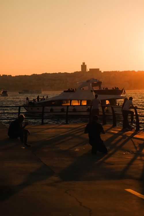 Free A serene sunset at the harbor with silhouettes of people and boats, creating a tranquil scene. Stock Photo