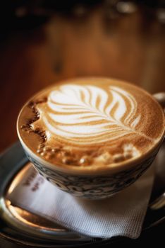 Close-up of a beautifully crafted leaf latte art in a detailed ceramic cup on a wooden table.