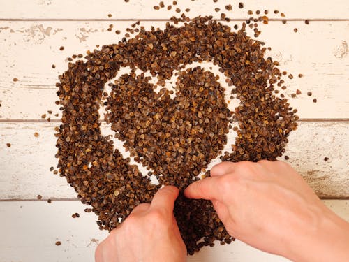 Free Female drawing a heart symbol in the pile of organic buckwheat husks on a wooden planks background Stock Photo