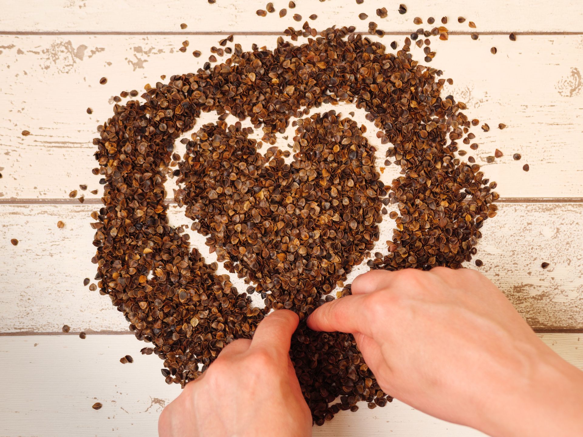 Female drawing a heart symbol in the pile of organic buckwheat husks on a wooden planks background