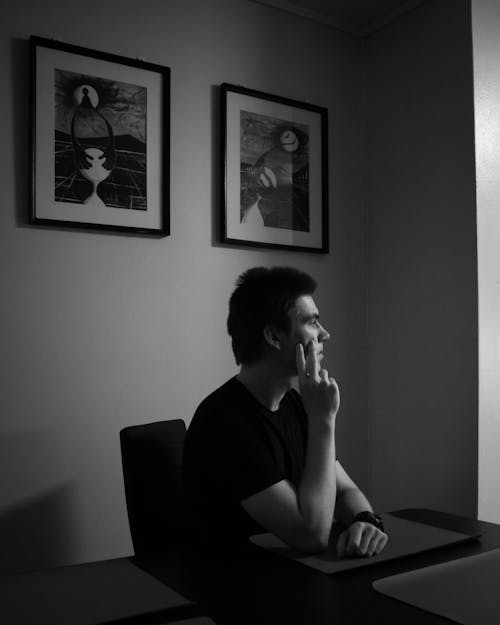 Grayscale Photo of Man Sitting Looking Afar 