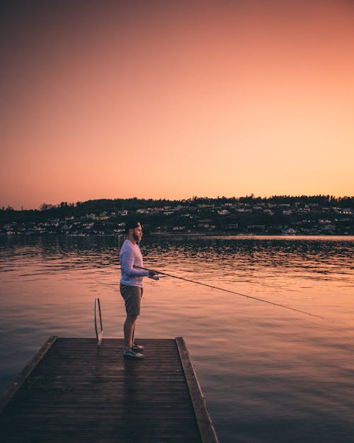 Man Standing on Wooden Dock While Fishing