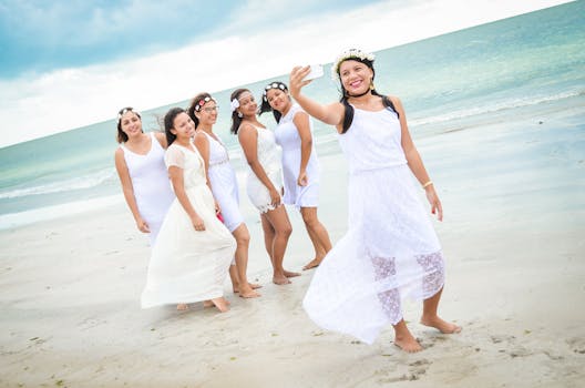 Group of women in white dresses taking selfies on a sandy beach in Recife, Brazil.
