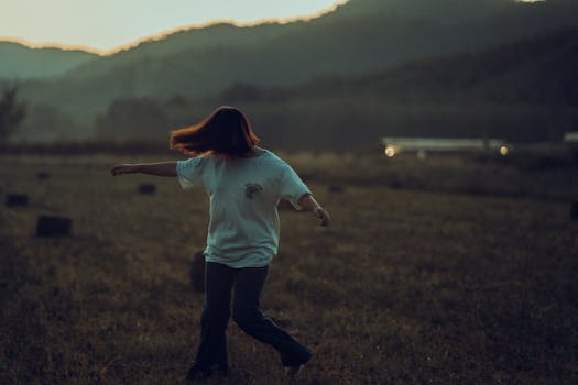 A youthful woman twirls in an open field during sunset, displaying a sense of freedom and joy.