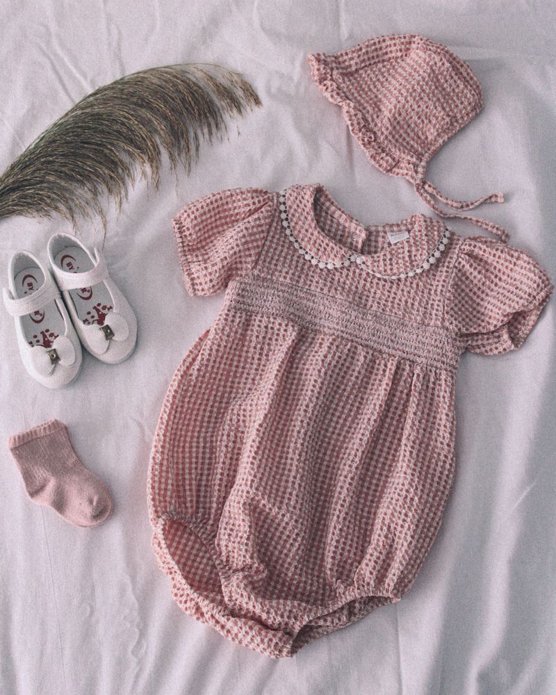 Gingham-weave cotton baby romper with matching bonnet, laid flat — photo by Fatma Gül on Pexels