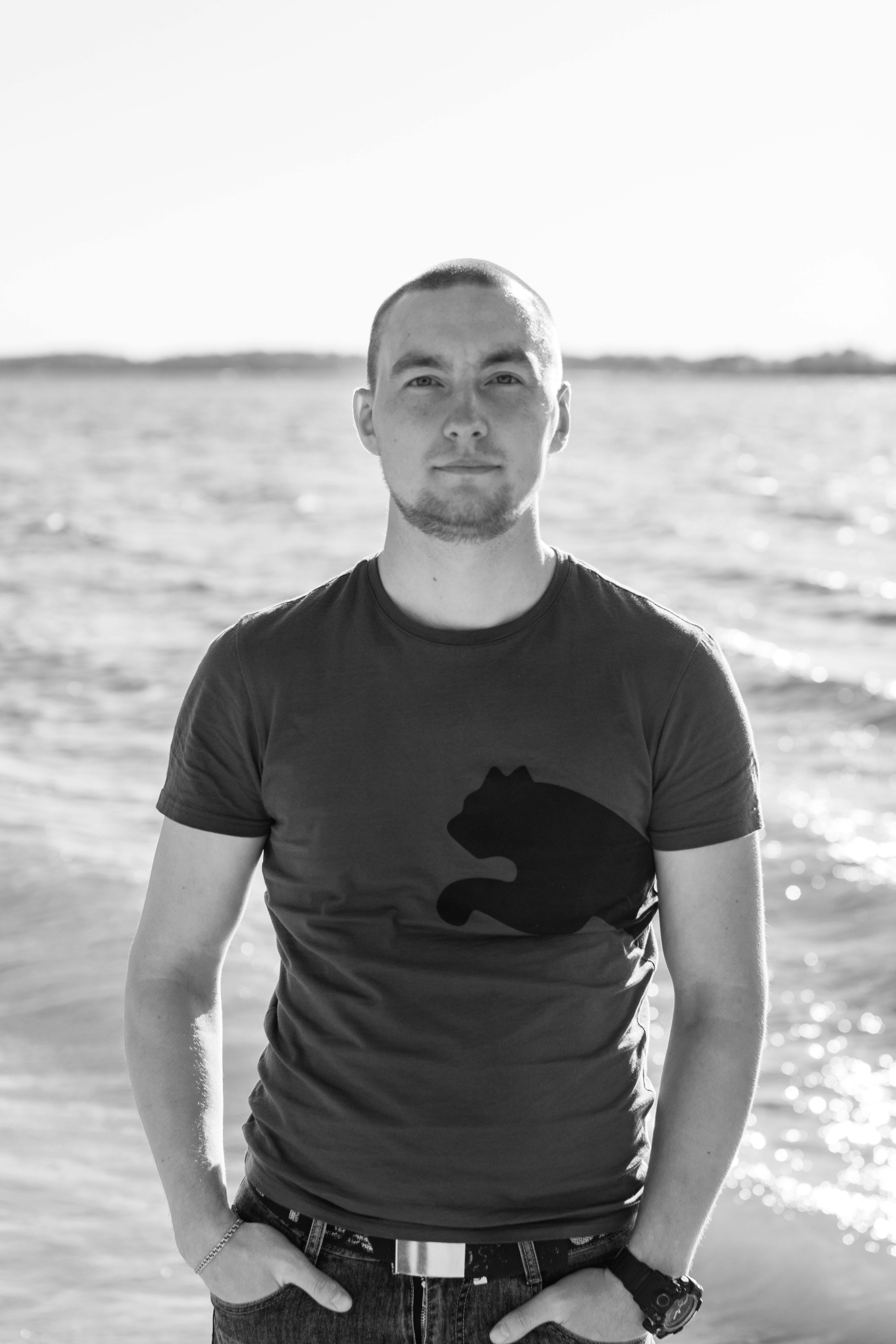 Black and white portrait of a man standing by the ocean on a sunny day.
