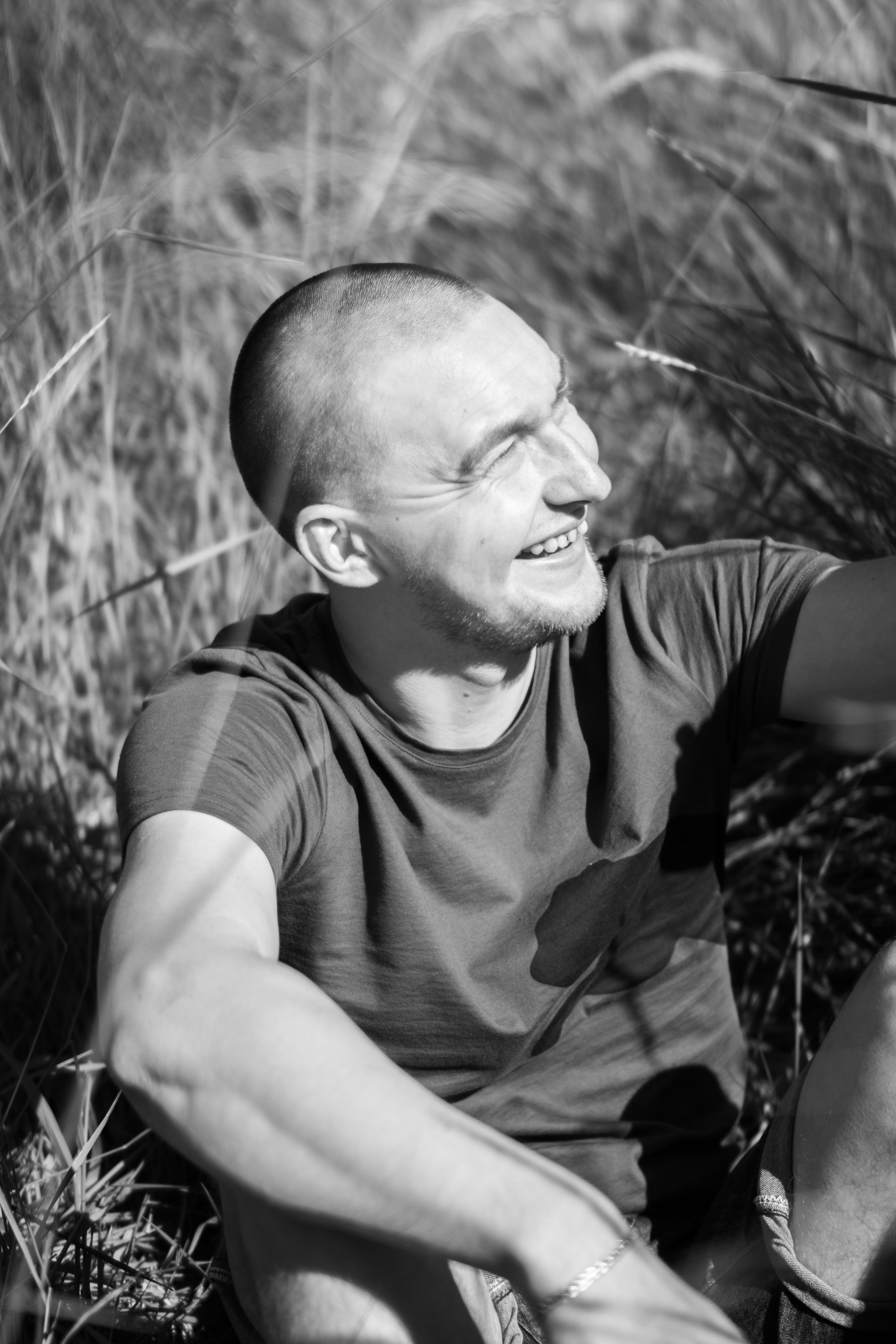 Black and white portrait of a man smiling while sitting in a grassy field.