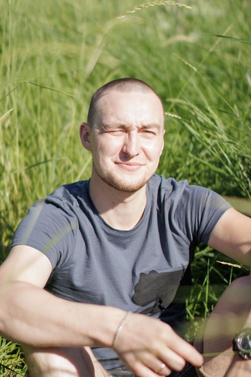 Free A man with a shaved head enjoys the sun in a lush green field, smiling contentedly. Stock Photo