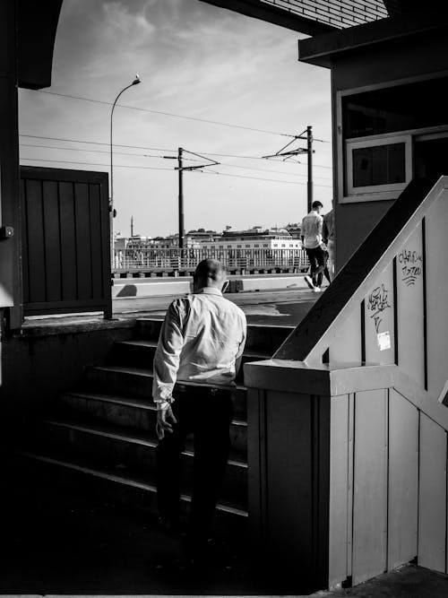 Black and White Photo of a Man Walking Towards the Stairs