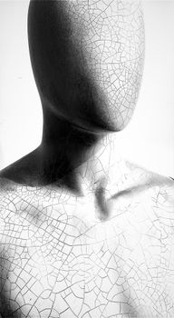 Black and white close-up of a cracked, faceless mannequin with an artistic flair.