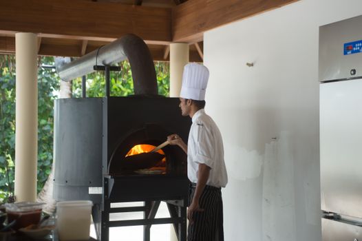 A chef prepares food using a traditional pizza oven indoors, showcasing culinary expertise.