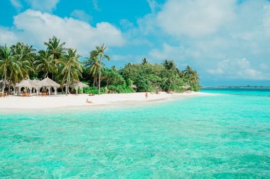 A beautiful tropical beach with turquoise water, palm trees, and white sand under a blue sky.