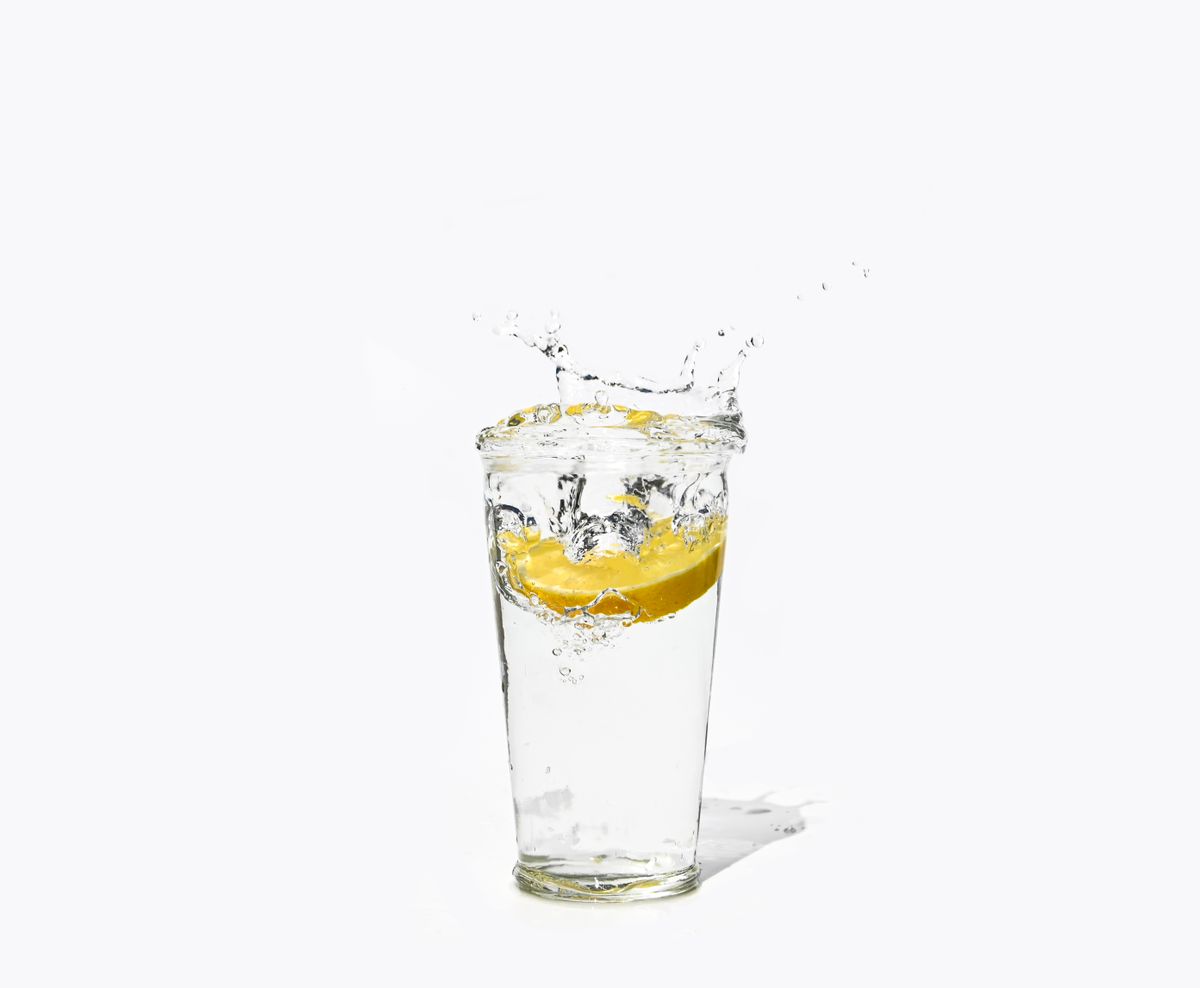 A tall glass of water with a slice of lemon dropped in, splashing on a white background