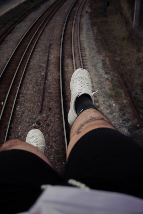 Person in Black Shorts and White Sneakers Near Train Track 