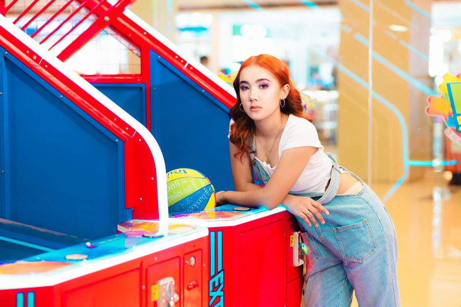 Stylish young woman leaning on a colorful arcade game in an amusement arcade setting. Stylish young woman leaning on a colorful arcade game in an amusement arcade setting.